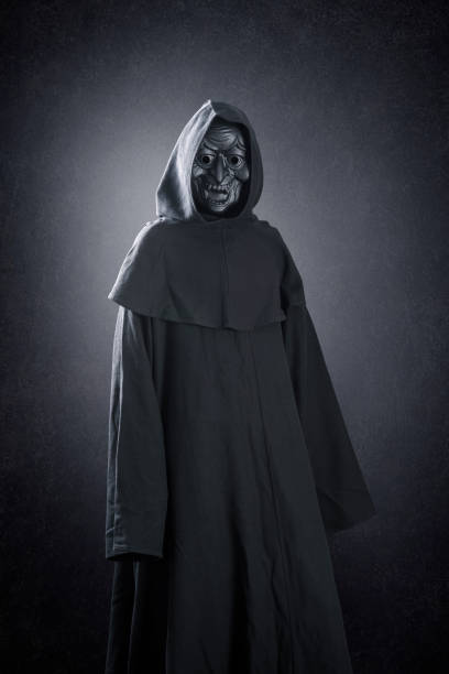 istock Spooky figure with hooded cape over dark misty background 1349392224
