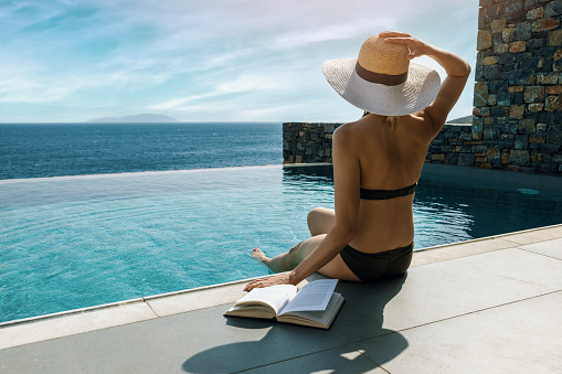 woman sunbathing and relaxing by the swimming pool with sea view in luxury villa