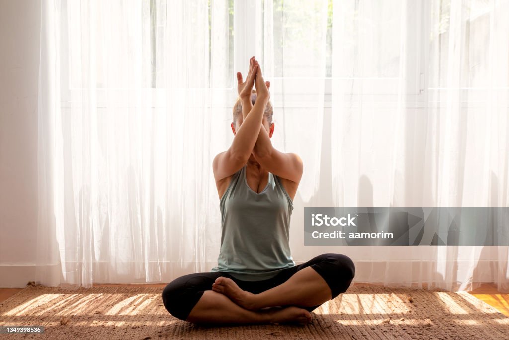 Relaxed woman with closed eyes practicing yoga in lotus position in the living room 45-49 Years Stock Photo