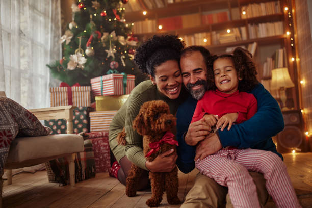 Mixed race family celebrating Christmas at home Excited girl and her family sitting on the floor near christmas tree and smiling. Mixed race family during Christmastime family christmas stock pictures, royalty-free photos & images