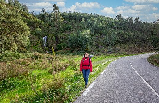 A woman tourist, in a jacket, hitchhiking on the road, walks along the Portuguese forest roads. Stops fellow travelers. High quality photo