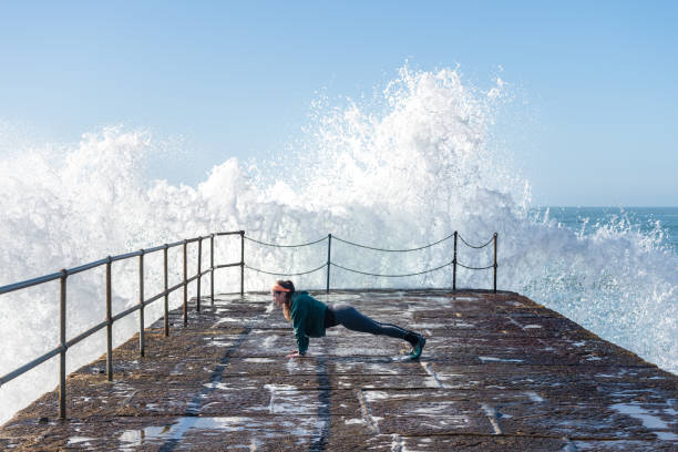istock Woman doing yoga pose on harbour whilst wave crashes against wall. 1349410390