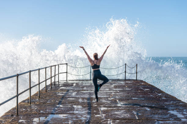 istock Woman practicing yoga on harbour with crashing waves. 1349410432