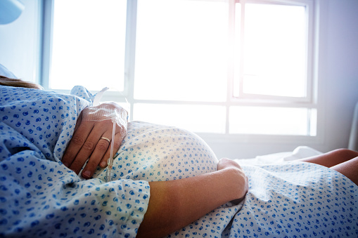 Close-up of a pregnant woman's belly in the hospital bed with catheter in hand