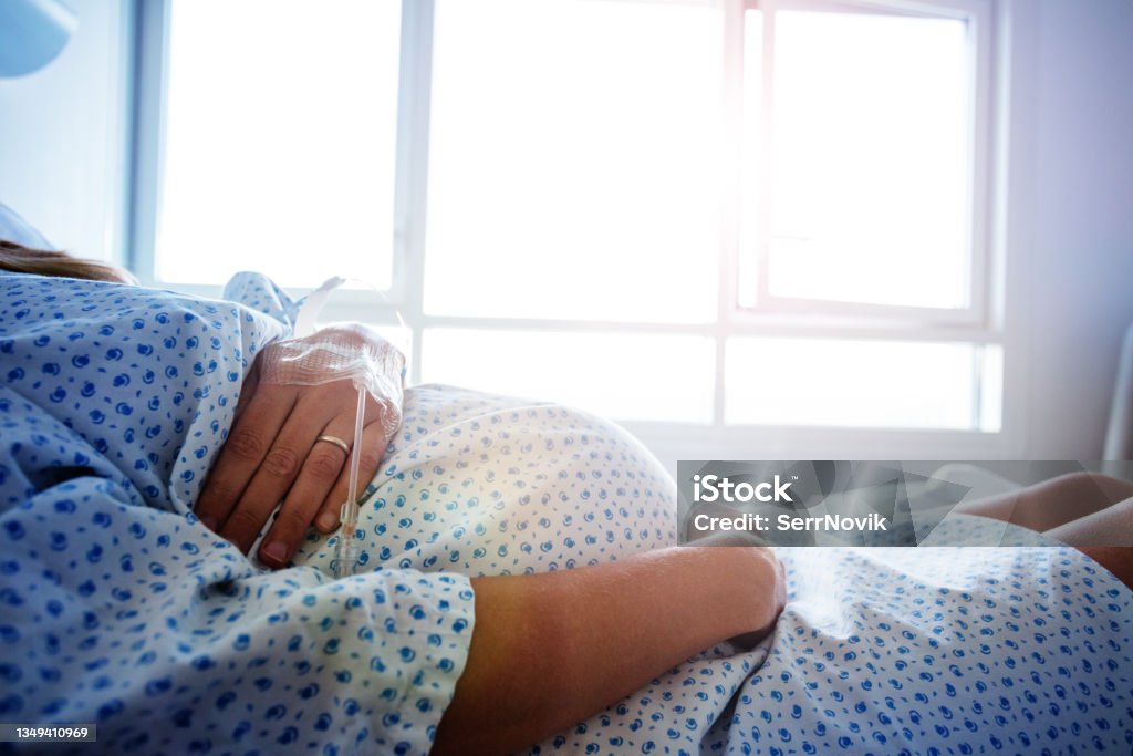 Close-up of a pregnant woman's belly in hospital Close-up of a pregnant woman's belly in the hospital bed with catheter in hand Pregnant Stock Photo