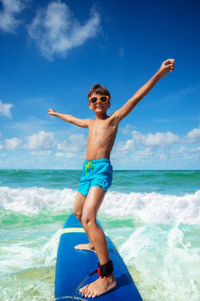 istock Cute happy boy riding surfboard in sea lift hands 1349411954