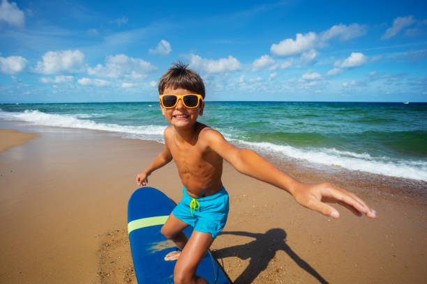 Portrait of a boy in action pose training to position on the surfboard - fun during summer camp on the beach