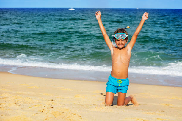 Happy boy on the beach wearing snorkeling mask happily lift hands up