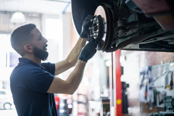 young mechanic checking the brake disk of a car on lift at the workshop - travão imagens e fotografias de stock