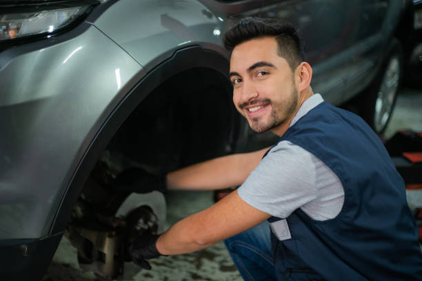 Friendly mechanic checking the car disk of the front wheel facing camera very cheerfully - Car industry concepts