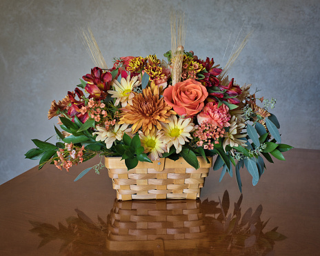 A beautiful fall flower arrangement reflecting on a polished wood table.