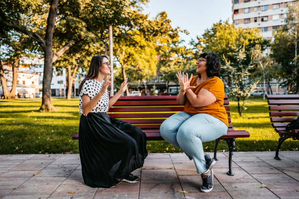 Two deaf and hard hearing women speak in sign language outdoors.