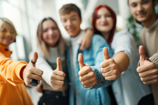 Thumbs up! Closeup front of a group of high school students on a break between classes showing thumbs up to the camera. high school building stock pictures, royalty-free photos & images
