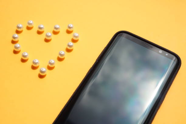 istock Black smartphone and pearl beads on an orange table. 1349424421