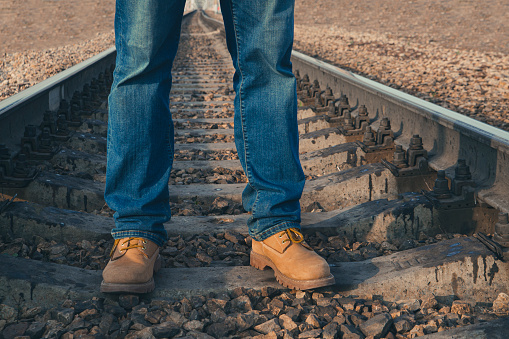 A guy in jeans and yellow boots stands on the railroad tracks. Railway transport, travel, communications.