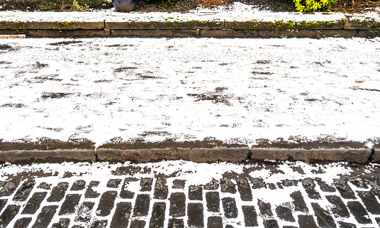 Side view of a pavement covered in ice and snow, making for slippery and dangerous conditions for pedestrians.
