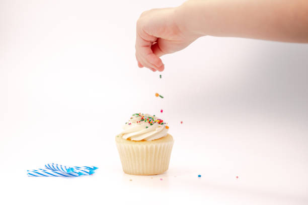 istock Child's hand decorating a cupcake with sprinkles and birthday candles 1349431571
