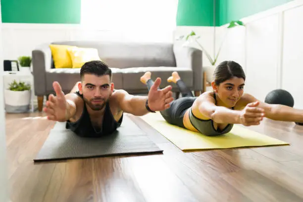 Attractive workout partners in a locust pose working out with yoga exercises in the living room