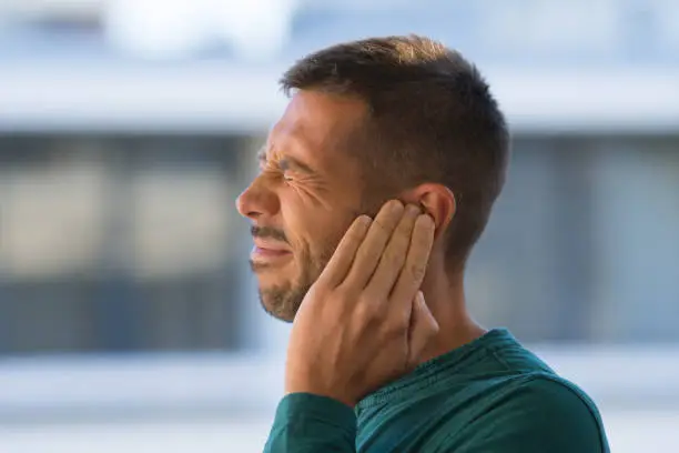 Otitis or tinnitus. Man touching his ear because of strong earache or ear pain. . High quality photo