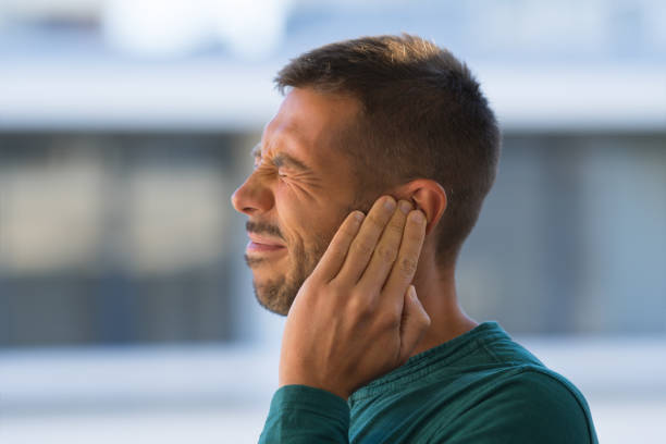 otitis or tinnitus. man touching his ear because of strong earache or ear pain. - tinitus imagens e fotografias de stock