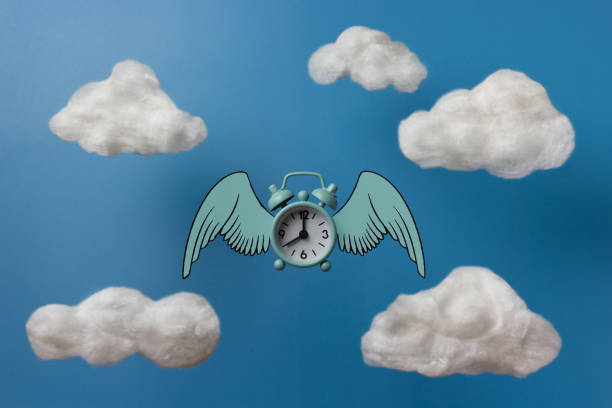 istock Flying blue alarm clock with wings under the clouds. 1349435198