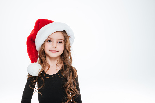 Portrait of beautiful curly little girl in santa claus hat over white background
