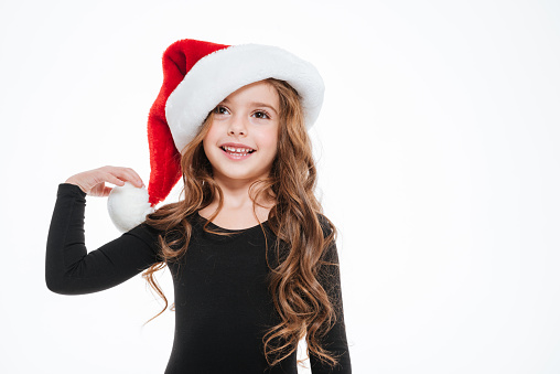 Happy pretty little girl in santa claus hat standing and smiling over white background