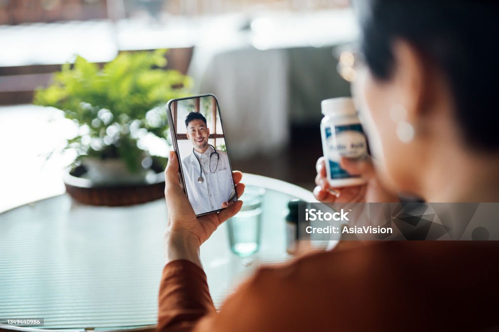 Senior Asian woman having a virtual appointment with doctor online, consulting her prescription and choice of medication on smartphone at home. Telemedicine, elderly and healthcare concept Telemedicine Stock Photo