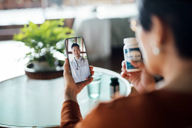 Senior Asian woman having a virtual appointment with doctor online, consulting her prescription and choice of medication on smartphone at home. Telemedicine, elderly and healthcare concept stock photo