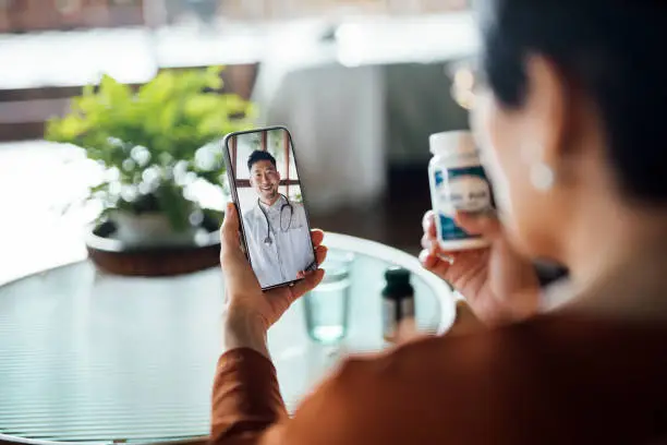 Photo of Senior Asian woman having a virtual appointment with doctor online, consulting her prescription and choice of medication on smartphone at home. Telemedicine, elderly and healthcare concept