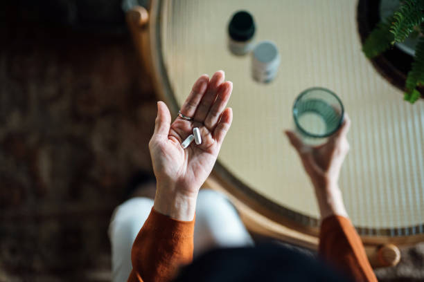 vue aérienne d’une femme asiatique âgée se sentant malade, prenant des médicaments à la main avec un verre d’eau à la maison. concept pour les personnes âgées et les soins de santé - water human hand people women photos et images de collection