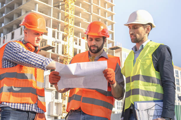 istock Business Engineers looking at blueprints. Male workers engineers at construction site in helmets hardhats near high-rise building skyscraper. 1349441148