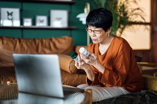 Senior Asian woman having a virtual appointment with doctor online, consulting her prescription and choice of medication on laptop at home. Telemedicine, elderly and healthcare concept
