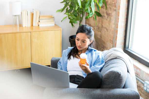Woman uses tele-health on laptop to talk to pharmacist The mid adult woman holds a prescription pill bottle and uses a tele-health app on her laptop to talk to her pharmacist. Pharmacy stock pictures, royalty-free photos & images