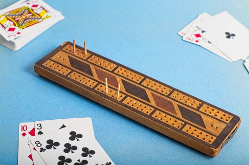 Vintage wooden cribbage board and playing cards on blue background. Cribbage is a classic fast scoring card game with a board and pegs to keep score. Its origins date from the 17th Century.