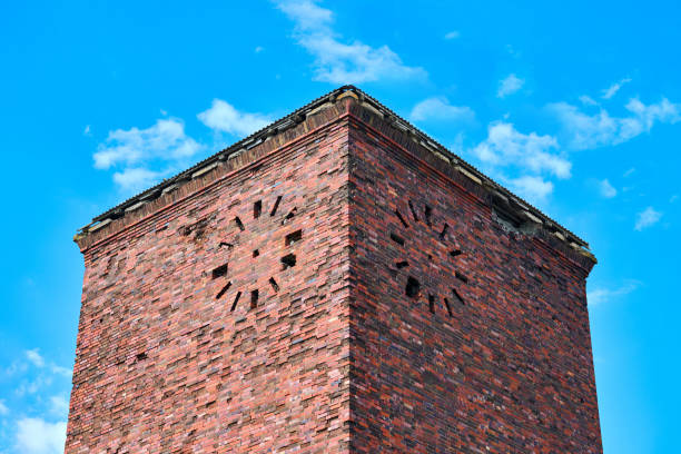 Old abandoned red brick tower with round clock on facade against blue sky background, fragment. Vintage grain brick masonry industrial building, ancient architecture backdrop