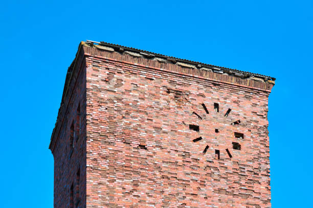 Old abandoned red brick tower with round clock on facade against blue sky background, fragment. Vintage grain brick masonry industrial building, ancient architecture backdrop