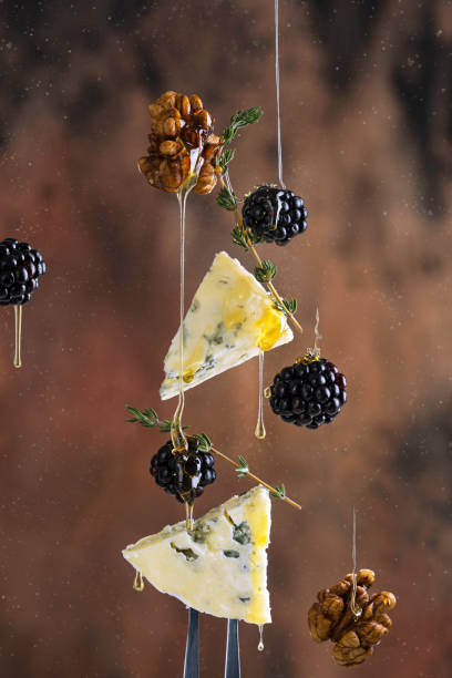 Slices of blue cheese with fresh berries - blackberries, honey, herbs and walnuts - levitation art conceptual studio photo Slices of blue cheese with fresh berries - blackberries, honey, herbs and walnuts - levitation art conceptual studio photo, macro shot. Wooden brown background, copy space. blue cheese stock pictures, royalty-free photos & images