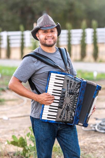 카우보이 모자를 쓰고 목장에서 아코디언을 연주하는 성숙한 멕시코 농업 노동자 미소 - aliens and cowboys 뉴스 사진 이미지