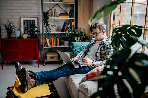 Shot of a man using a laptop and credit card on the sofa at home