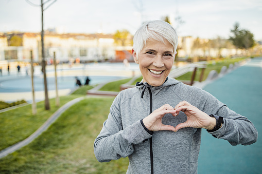 Portrait of smiling senior woman with short hair in sports clothing making a heart sign with her hands