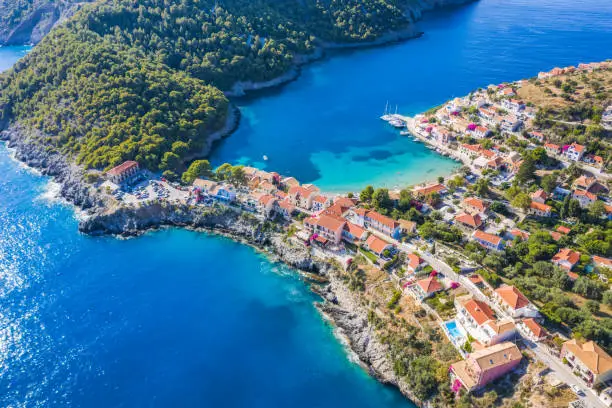 Assos picturesque fishing village from above, Kefalonia, Greece. Aerial drone view. Sailing boats moored in turquoise bay.
