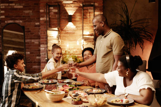 African American Family Celebrating at Dinner Warm toned portrait of happy African-American family clinking glasses and toasting while enjoying dinner together at evening black people eating stock pictures, royalty-free photos & images