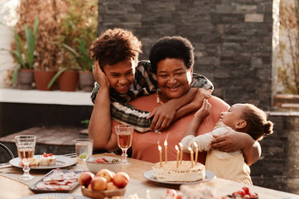 Happy Grandmother Playing with Children Portrait of two African-American kids embracing grandmother during family dinner outdoors lit by sunlight happiness four people cheerful senior adult stock pictures, royalty-free photos & images