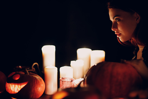 Young woman making Halloween pumpkin Jack-o-lantern with candles in dark
