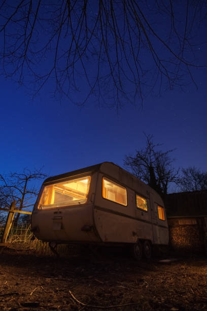 istock Old white caravan trailer with yellow illumination in backyard at stary blue night 1349485703