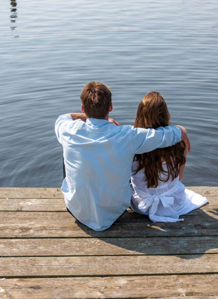 istock embracing couple sitting on pier at waterfront 1349485764