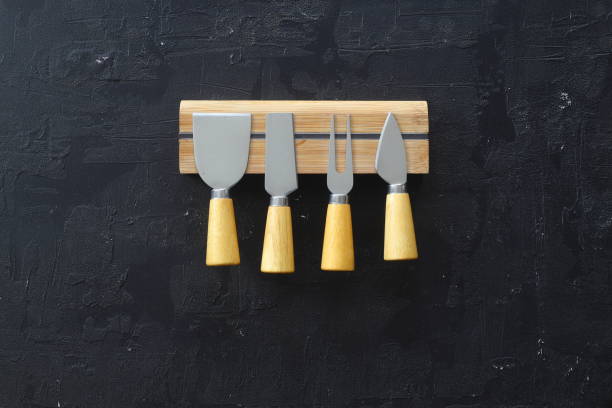 Cheese knives and fork on black background, flat lay