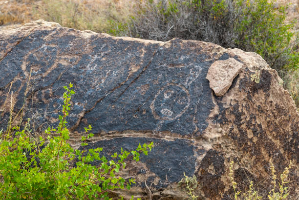 Kachina Symbol Carved in Rock Indigenous people have been carving in rock for thousands of years as a means of written communication.  Petroglyphs are either images, designs or symbols chiseled, carved or scratched on the surface of the rock.  Many of these carvings have endured over the centuries and are still visible today.  The image on the right side of this rock depicts a round face.  Modern natives in this area identify this as a Kachina, or spirit being.  Research suggests that the Kachina Culture came to this area around 1300AD.  Similar Kachina symbols are used in modern Puebloan pottery and weavings which helps make the connection from past to present.  We don’t always know the true meaning of these carvings or how to interpret them.  And maybe it’s not our place to try.  We can however enjoy them for their artistry.  These petroglyphs were photographed at Puerco Pueblo in Petrified Forest National Park near Holbrook, Arizona, USA. jeff goulden petrified forest national park stock pictures, royalty-free photos & images