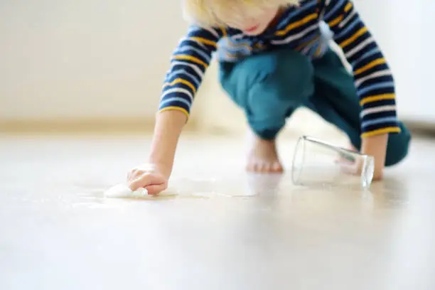 Photo of Little boy wipes water spilled from a glass on the floor. Teaching a child to clean up after himself. Responsibility, accuracy.